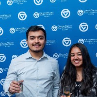 A girl and boy posing in front of the GVSU Alumni backdrop